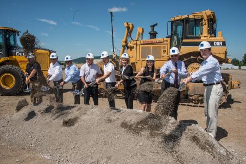 groundbreaking ceremony of Ecopax Inc manufacturing team wearing white safety helmets, shovelling dirt, and two yellow excavator truck